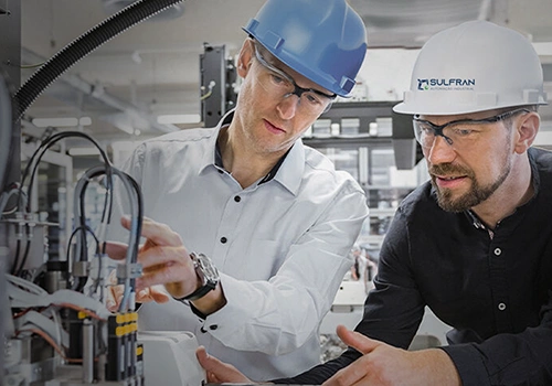 Dois engenheiros inspecionando fiação em equipamento industrial.